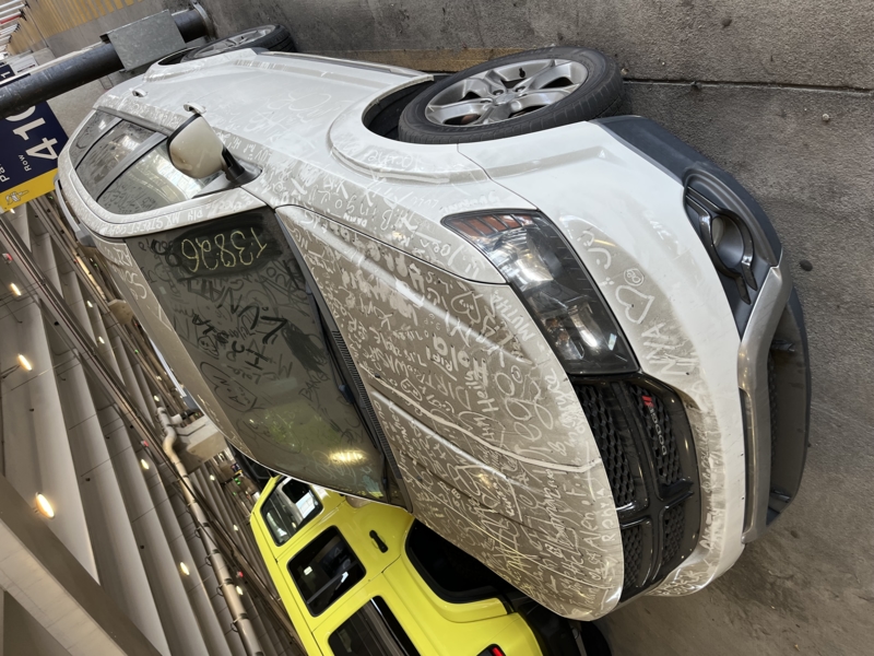 A white car, covered in dust and drawings made in dust.