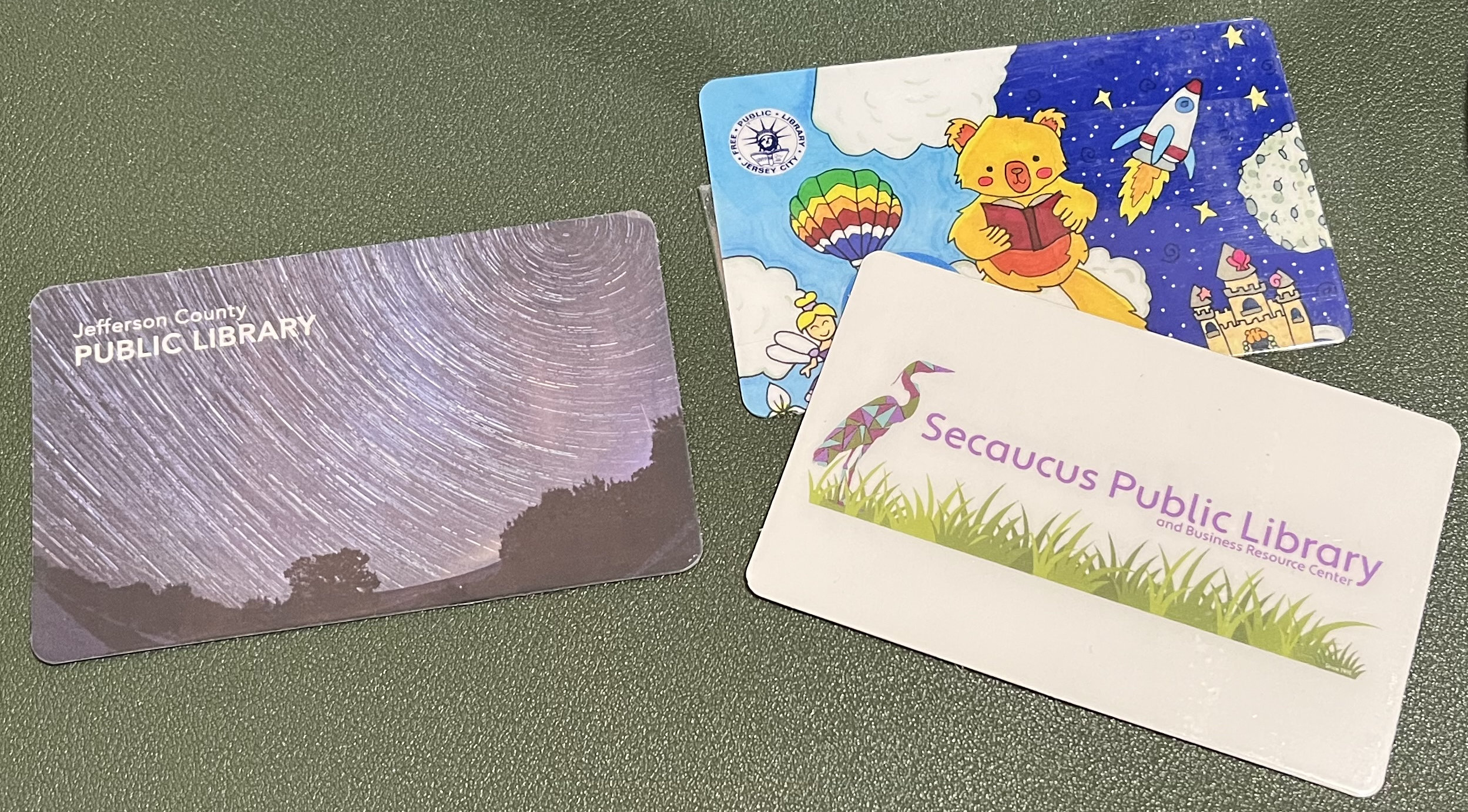 Three library cards on a desk: Jefferson County, JCPL, and Secaucus.
